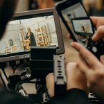 A photographer captures a video on a smartphone and monitor inside a studio setting.